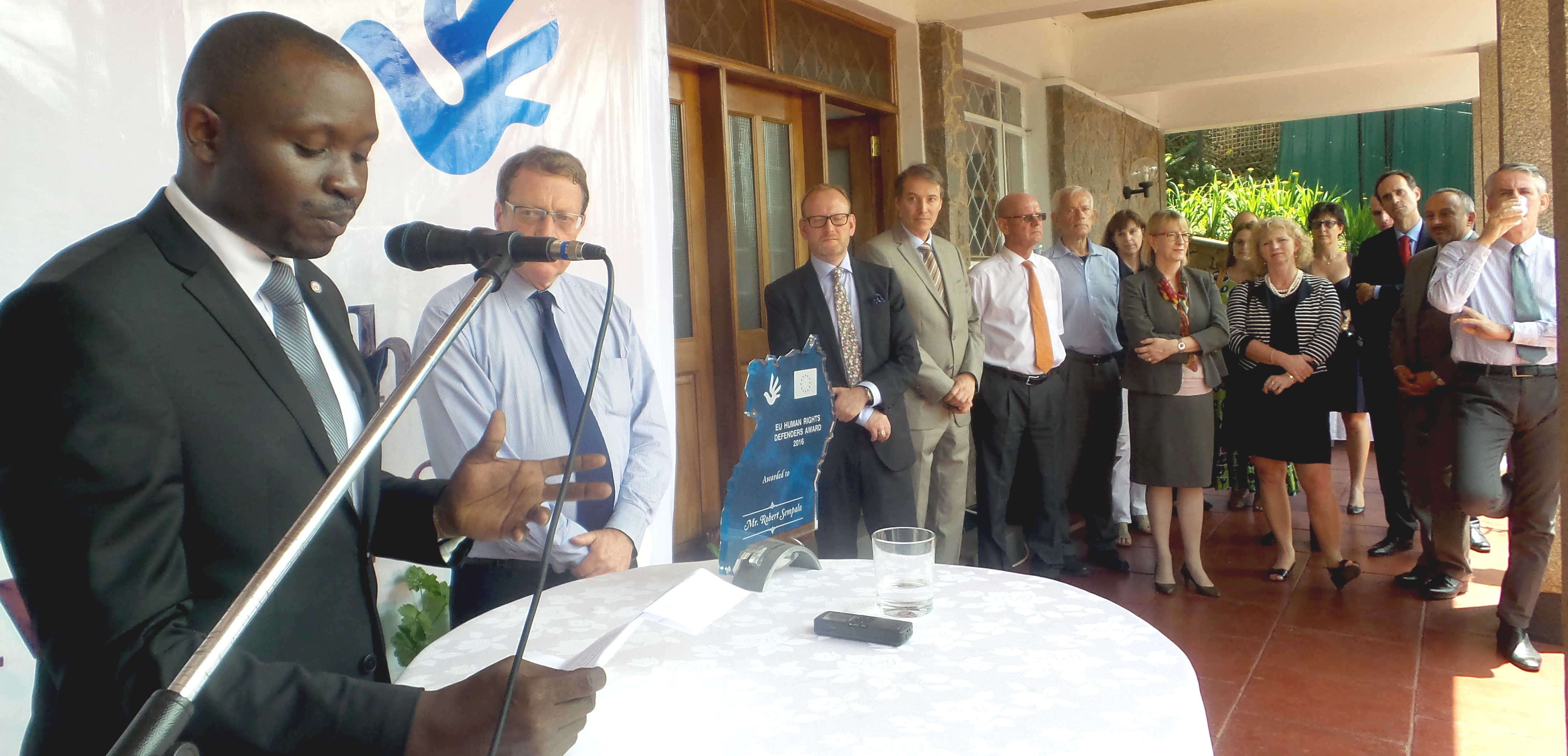 HRNJ Coordinator Robert Ssempala making remarks after receiving the award. Listening are EU region envoys in Uganda