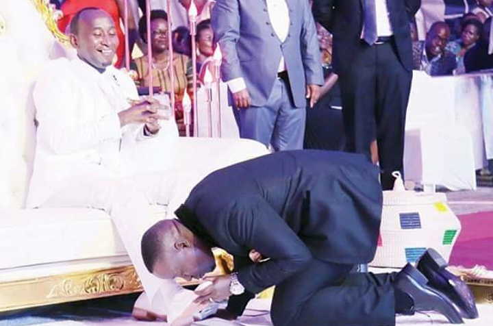 Prophet Mbonye, seated and dressed all in white enjoying the way a follower kisses his shoe at a recent ceremony